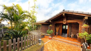 Une cabane en rondins de bois dotée d’un patio carrelé, entourée d’une clôture en bois et agrémentée de différents pots de plantes.