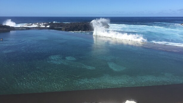 On peut clairement voir un grand bassin d’eau calme, avec des vagues qui se brisent contre une côte rocheuse.