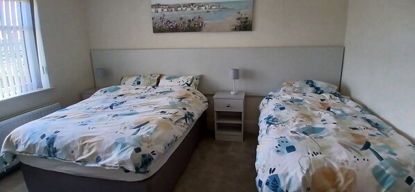 A bedroom with two beds, a nightstand, a lamp, and a painting on the wall. - Amazing Sea views. Central location. Overlooking Portstewart Old Course. (Portstewart)