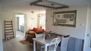 A dining area with a white table and chairs, a wooden ladder, and a kitchen in the background.