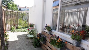 A small outdoor area with a wooden bench, a metal chair, and potted plants.