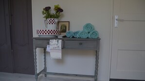 A small table with a vase, a framed picture, and rolled towels against a wall.