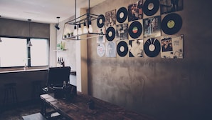 A room with a wooden table, bar stools, a hanging light fixture, and a wall adorned with vinyl records and posters. - See U Hostel Osaka (Osaka)