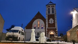 A church with a tall bell tower and a snow-covered fence in front.