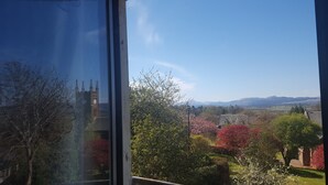 A view through a window with a clear sky, a church tower, and a landscape with trees and distant hills.
