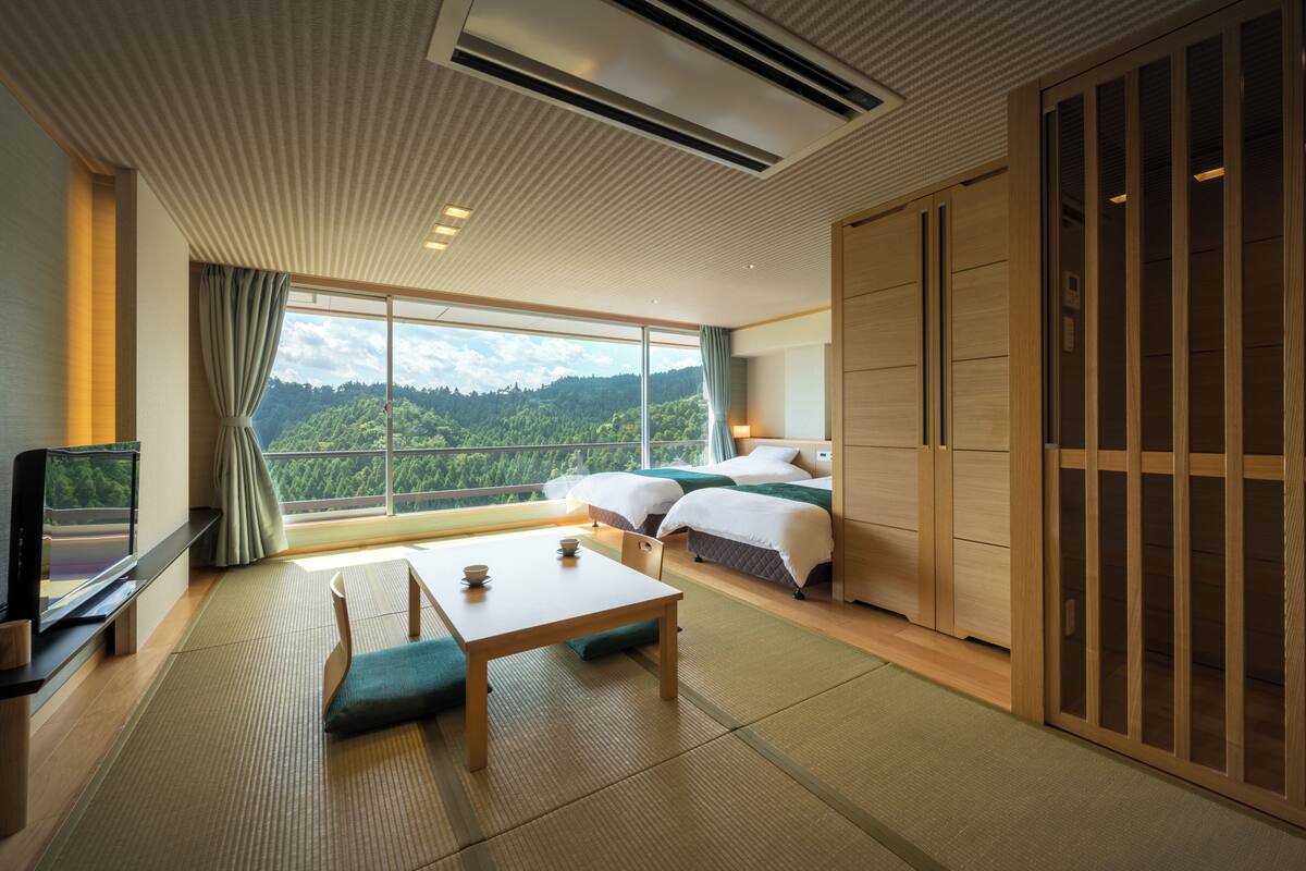 Une chambre d’hôtel moderne dotée d’une grande fenêtre offrant une vue panoramique, d’une télévision, d’une table à manger et de portes coulissantes traditionnelles de style japonais.
