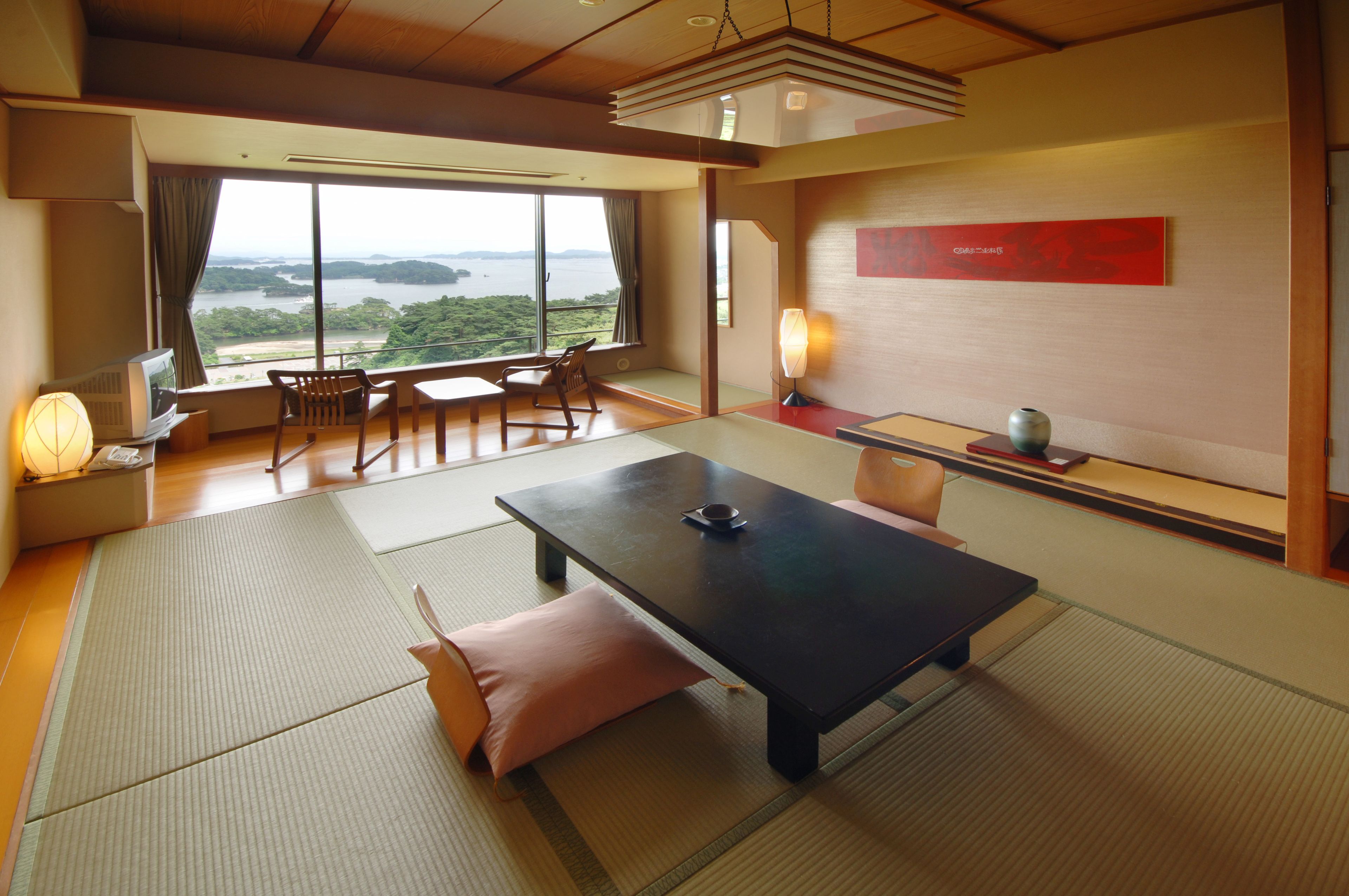 Une pièce de style japonais traditionnel, avec un sol recouvert de tatamis, une table basse et une vue sur un plan d’eau.