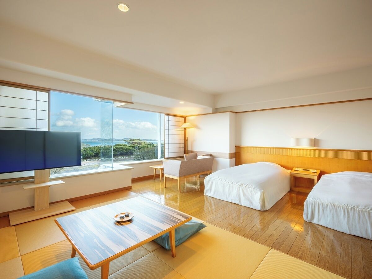 Habitación de hotel con una ventana grande, televisión de pantalla plana, cama, mesita de noche y una silla.