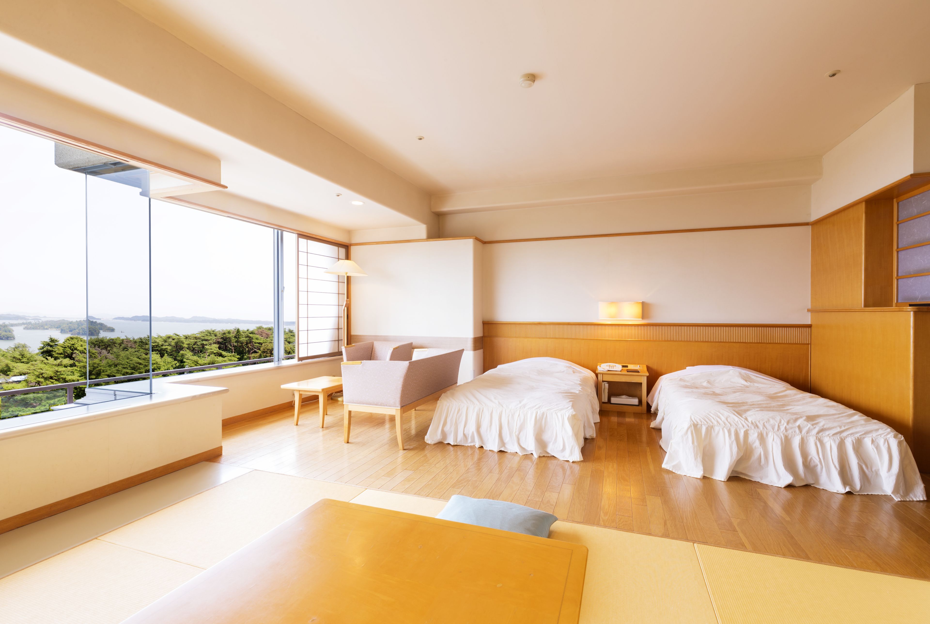 A modern hotel room with a large window, a sofa, two beds, and a wooden floor.