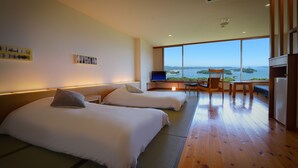 Een hotelkamer met twee bedden, een bureau met stoel, een televisie en een groot raam met uitzicht op zee.
