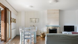 A modern living room with a fireplace, a dining area with white chairs, and a television on a stand. - Nice Stay B Paz: 2 terraces with incredible views. Wifi, BBQ, swimming pool, paddle. (Panticosa)