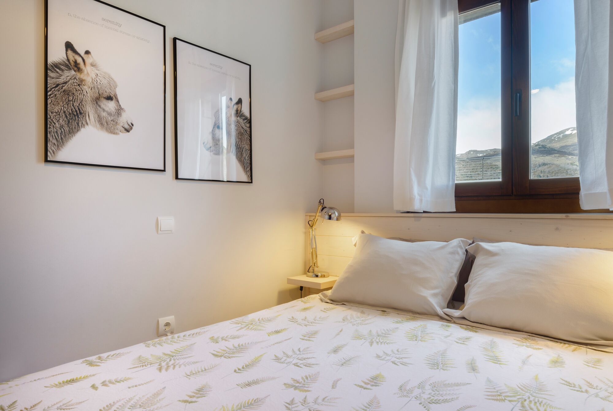 A bedroom with a bed, a nightstand, a lamp, and two framed pictures on the wall.