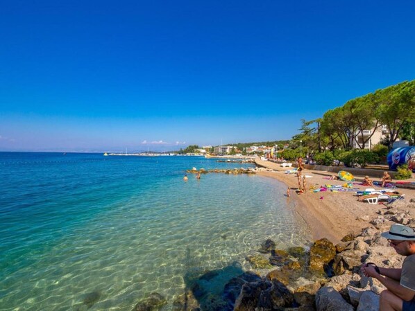 Relax on the beach with umbrellas and sun loungers, surrounded by clear blue waters and a natural rocky coastline.
