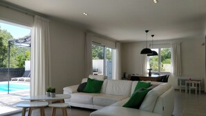 Un salon moderne avec un canapé blanc, deux petites tables rondes et un coin repas comprenant une table et des chaises.