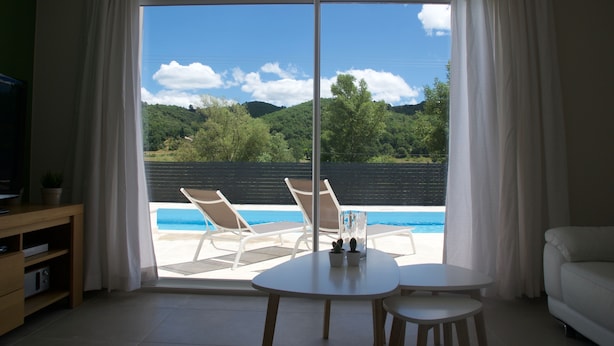 Une pièce dotée d’une grande porte-fenêtre coulissante donnant sur une zone piscine, d’un canapé blanc et d’une petite table avec deux chaises.