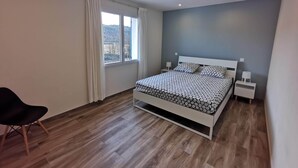 Une chambre moderne avec un lit, des tables de chevet, une chaise et une fenêtre avec des rideaux.