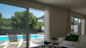 Un salon moderne avec une porte vitrée donnant sur une piscine, un canapé blanc et une petite table accompagnée de deux chaises.