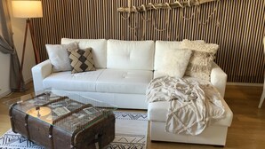 A white sofa with patterned cushions, a glass coffee table with a vintage trunk, and a bamboo wall panel. - Beautiful old building apartment in a top location 10 minutes to town in the residential area (Biederitz)