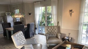 A spacious living room with a large window, a dining area, and a kitchen. - Fantastic 5 ***** Thatched cottage on the water with sauna, outdoor Jacuzzi, fireplace u. v. (Fuhlendorf)