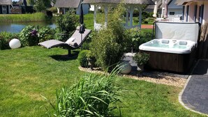 A well-maintained garden with a hot tub, lounge chairs, and a gazebo. - Fantastic 5 ***** Thatched cottage on the water with sauna, outdoor Jacuzzi, fireplace u. v. (Fuhlendorf)