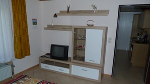 A room with a bed, a television, a cabinet with glass doors, and a door leading to a kitchen. - Apartment "Eifel Nest" between VULKANEIFEL and Moselle (Urschmitt)