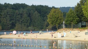A beach with people, tents, and a forested hill in the background.