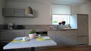 A modern kitchen with grey cabinets, a built-in oven, a coffee maker, a sink, and a window with blinds.