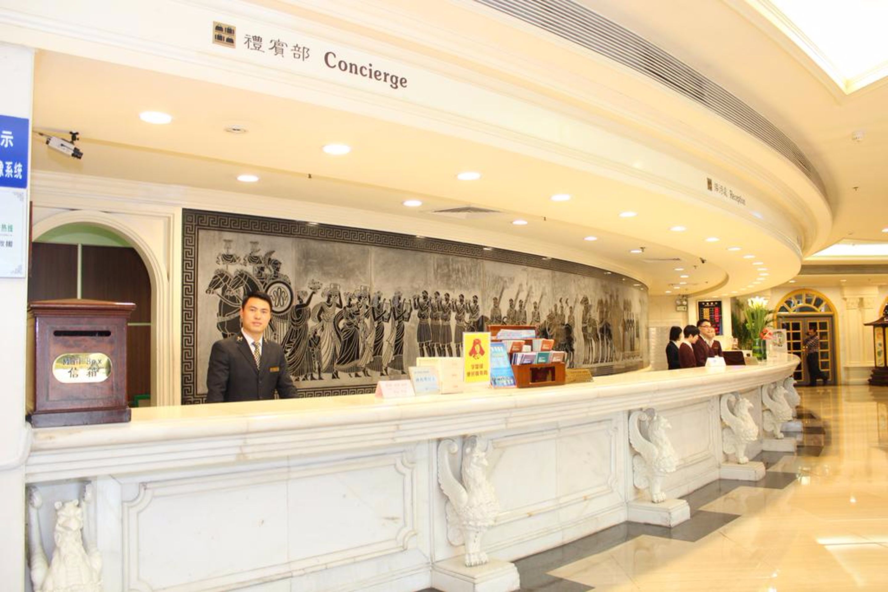 A hotel reception area with a large mural, a concierge desk, and a sign indicating the concierge service.