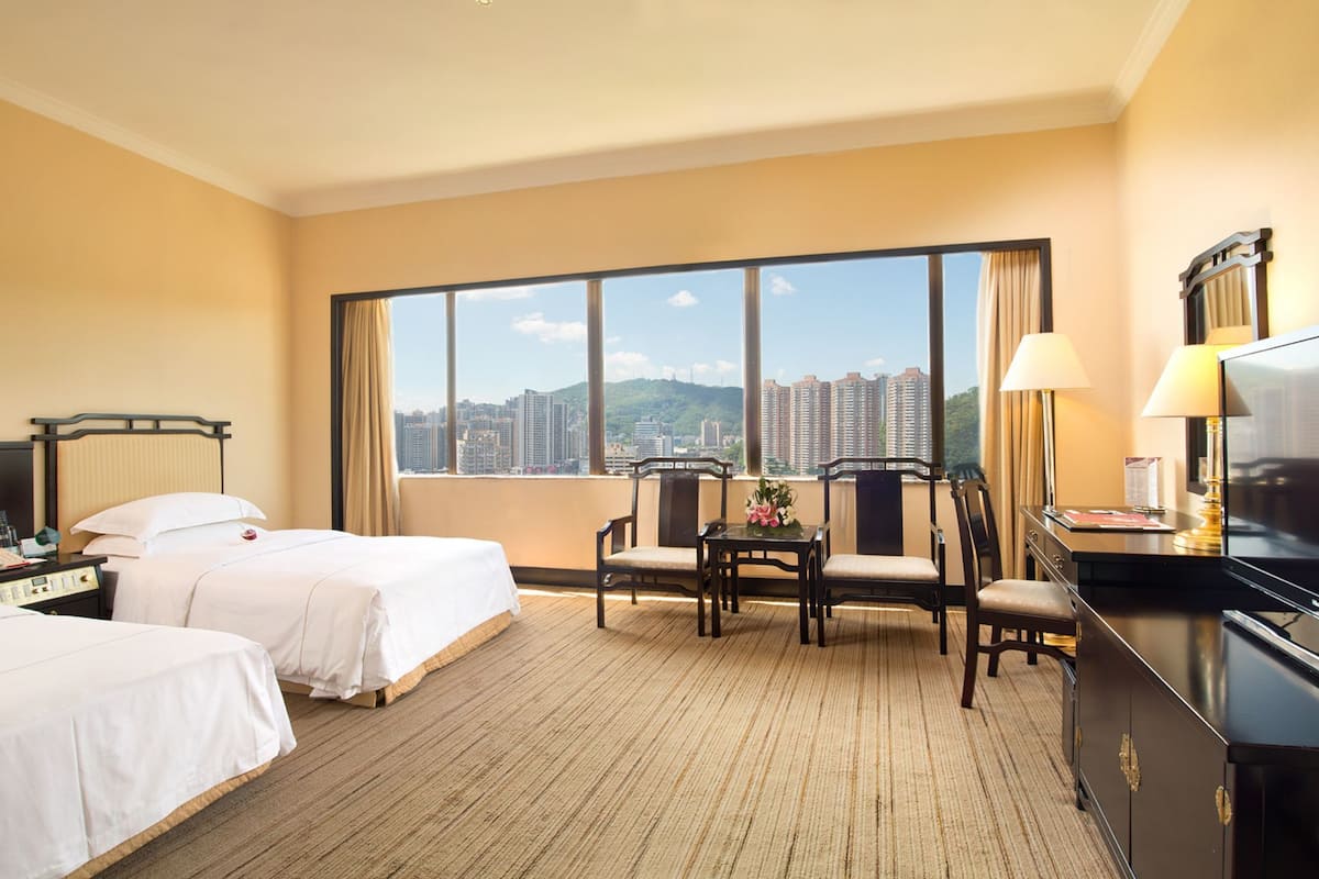 Une chambre d’hôtel avec deux lits, un bureau, une télévision et une grande fenêtre donnant sur la ville.