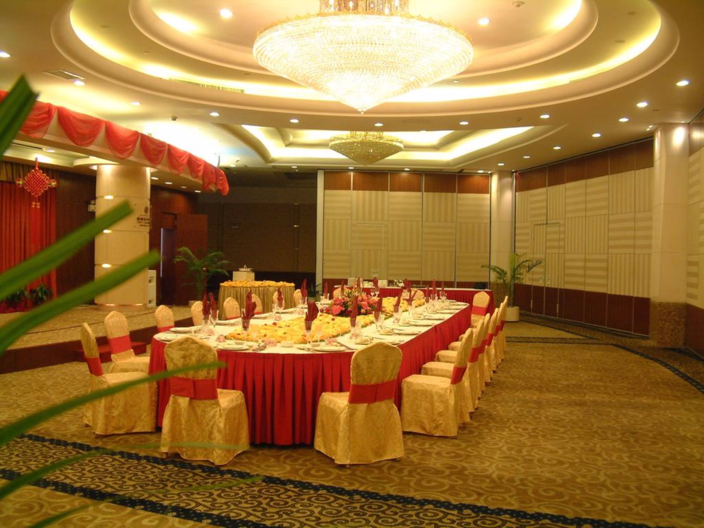 A banquet hall with a long table set for a formal event, surrounded by chairs with red sashes.