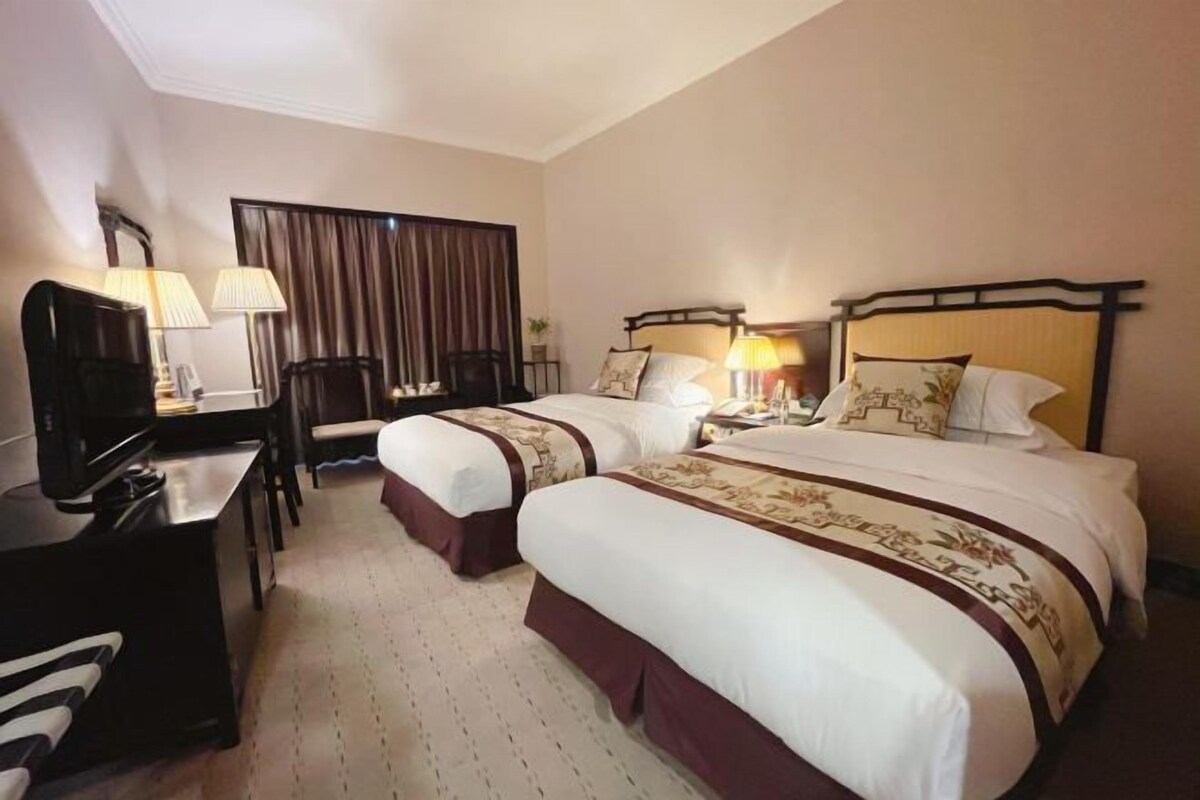 Habitación de hotel con dos camas individuales, un escritorio con silla, un televisor y una ventana con cortinas.