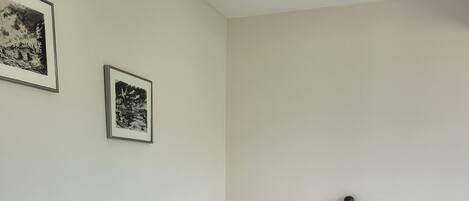 Quarto com cama, mesa de cabeceira com abajur e duas fotografias emolduradas na parede.