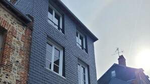 Un immeuble résidentiel de deux étages, à l’extérieur gris, avec des fenêtres à cadre blanc et une partie en briques sur le côté gauche.