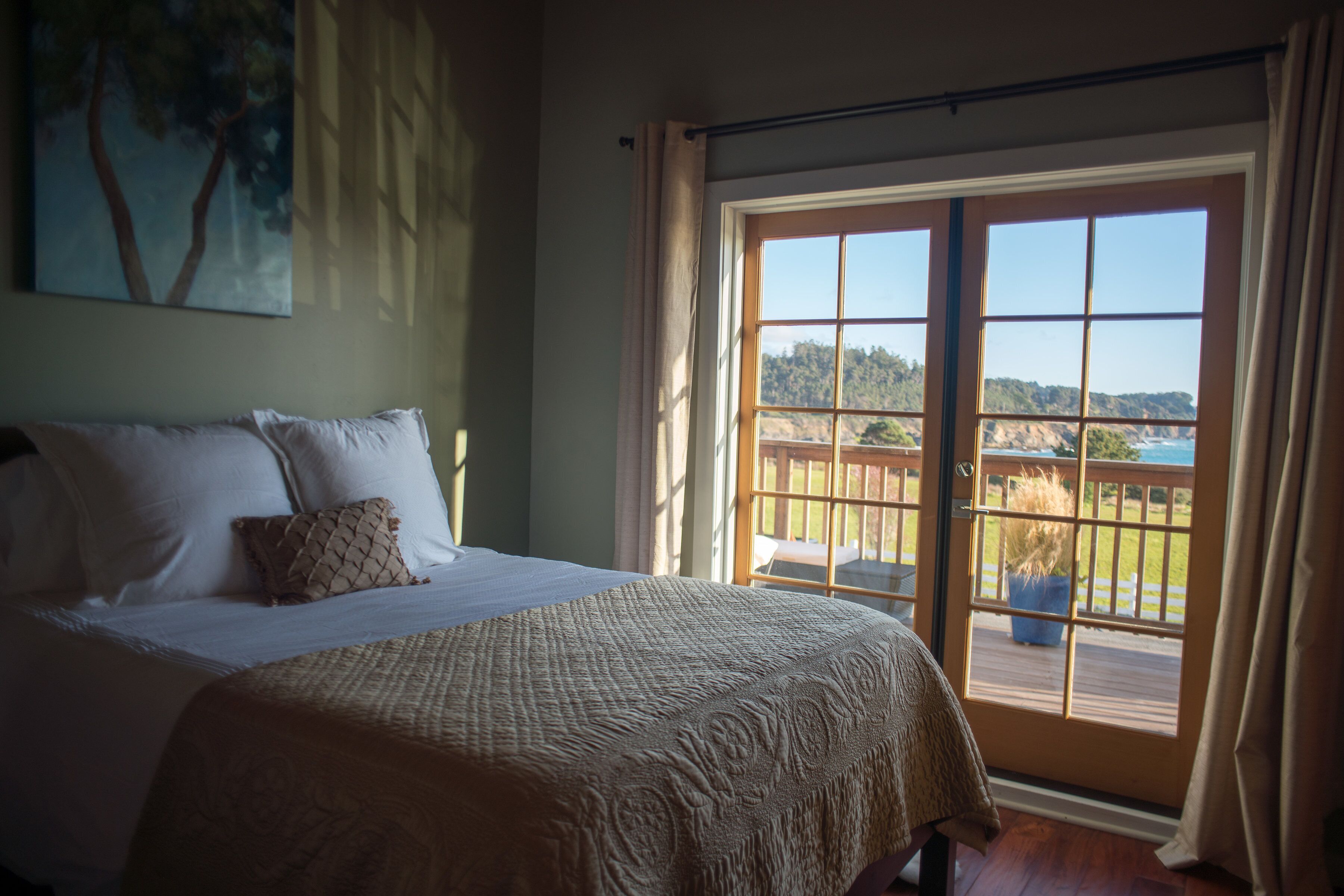 Un dormitorio con una cama grande, vistas a través de un ventanal corredero y un cuadro en la pared.