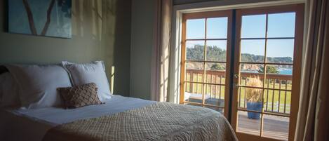 Un dormitorio con una cama grande, vistas a través de un ventanal corredero y un cuadro en la pared.