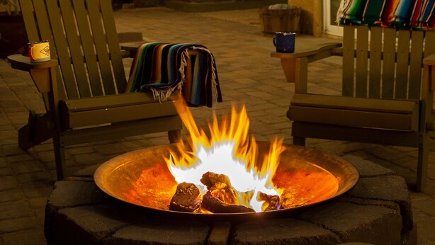 Un patio con una chimenea, mobiliario exterior e iluminación con luces colgantes.