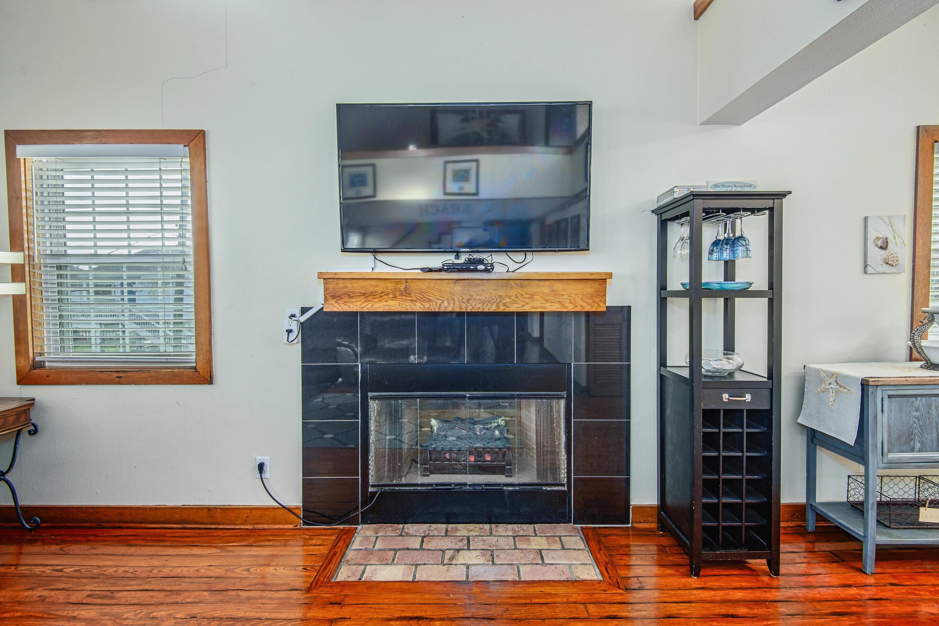 Una sala de estar con chimenea, un televisor montado encima y un mueble bajo con cristalería.