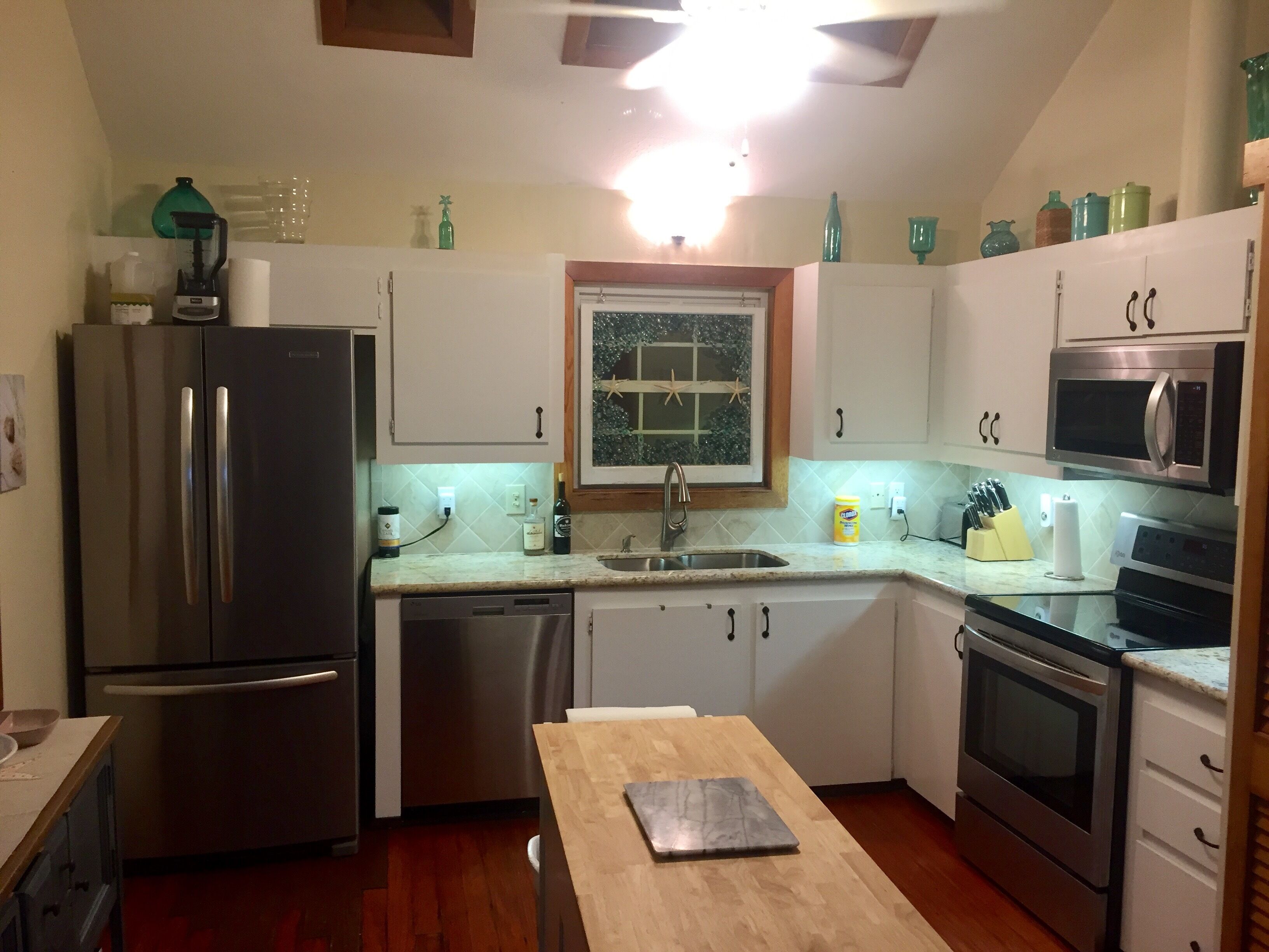 A compact kitchen with stainless steel appliances, a wooden table, and a window with a star decoration.