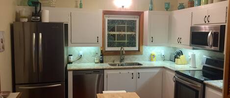A compact kitchen with stainless steel appliances, a wooden table, and a window with a star decoration.