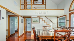 A spacious dining area with a wooden table and chairs, a staircase leading to a loft, and a large window with blinds.