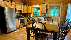 A wooden cabin kitchen with a dining table and chairs, stainless steel appliances, and wooden cabinets. - Creekside Log Cabin, Ideal Family Vacation! Hot tub, Fire Pit, Tubing, Fishing (Robbinsville)