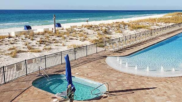 Una piscina con vista a la playa, un jacuzzi independiente y sillas de descanso a lo largo del borde de la piscina.