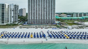 Un hotel frente a la playa con un edificio grande, una playa arenosa con hileras de sombrillas y una vista despejada del océano.