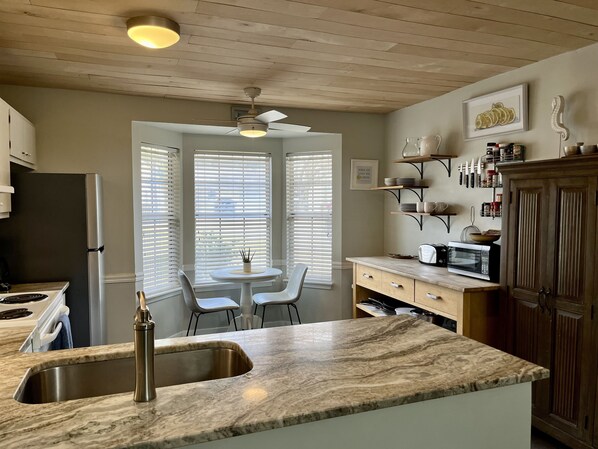 A kitchen with a marble countertop, a sink, a stove, and a ceiling fan. There is a window with blinds, a table with chairs, and a microwave on the counter. - August Sale!! Minutes from the islands, shops, parks, and downtown! (Mt Pleasant)