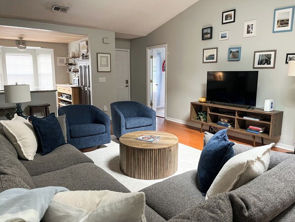 Una sala de estar con un sofá, dos sillones, una mesita de centro, un televisor y una estantería.