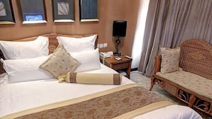 A neatly made bed with white linens and decorative pillows, a bedside table with a lamp, and a wicker sofa with cushions. - S&N Niutoushan Resort (Taizhou)