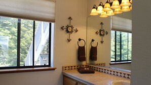 Une salle de bain avec un grand miroir, un lavabo et deux horloges fixées au mur.