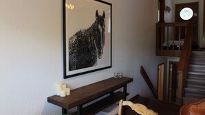 Un tableau en noir et blanc représentant un cheval, encadré et accroché au mur, un banc en bois avec des bougies et un escalier.