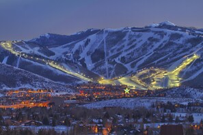 A snow-covered mountain landscape with a town at the base, illuminated by streetlights and buildings.