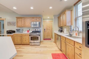 A modern kitchen with wooden cabinets, stainless steel appliances, and a red rug. - BEST Location Park City: Walk In Out Ski. Town, Trails, Garage (PARK CITY)